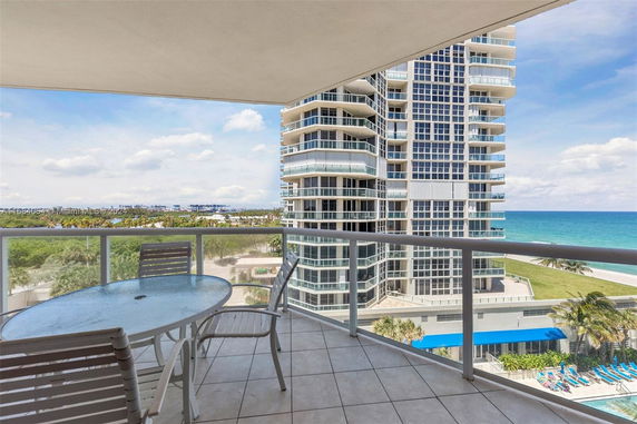Panoramic view from a balcony showing a tall modern building and the ocean.