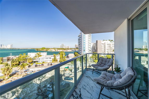 Balcony seating area with a view of the surrounding buildings and water.