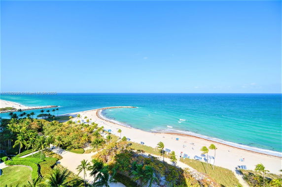 Panoramic view of a beach with clear blue ocean and sandy shore, surrounded by palm trees.