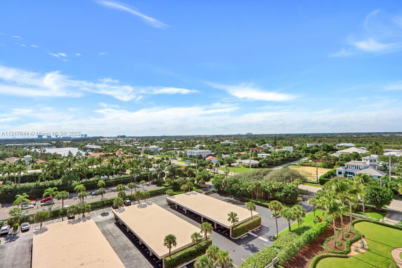 Aerial view showing residential area with houses, parking structures, and lush greenery.
