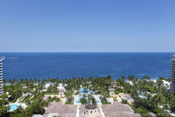 Aerial view overlooking palm trees, buildings, and a vast ocean backdrop.