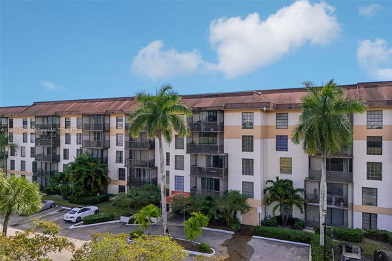Front view of a multi-story apartment building with balconies and palm trees in front.