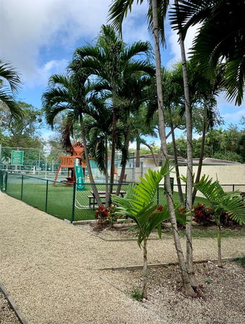 An outdoor play area with a fenced playground, greenery, and palm trees.