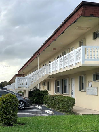 Front view of a two-story building with a staircase and a parking area.