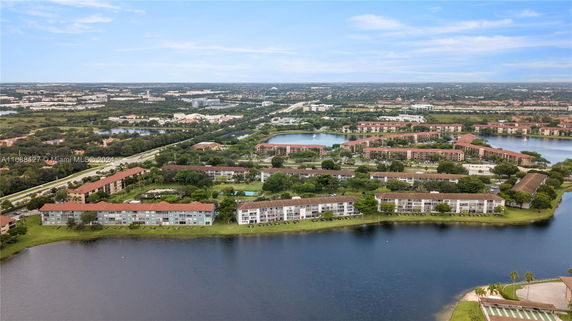 Aerial view of residential buildings with a lake in the foreground and surrounding landscape.