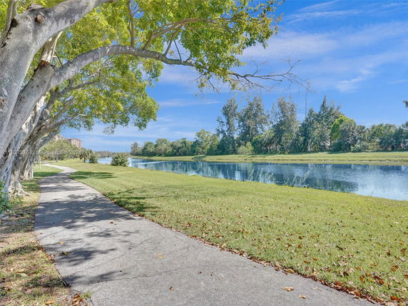 View of a walking path along a river with trees and grassy areas.