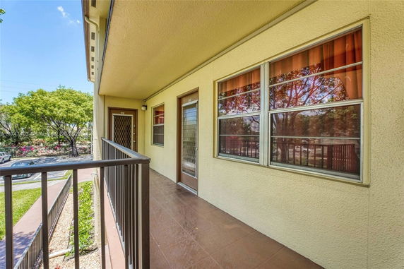 Exterior corridor of a residential building with windows and doors overlooking a landscaped area.