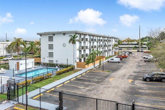 Multi-story apartment building with adjacent swimming pool and parking area.