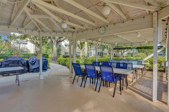 Outdoor covered seating area with tables and chairs, surrounded by greenery.