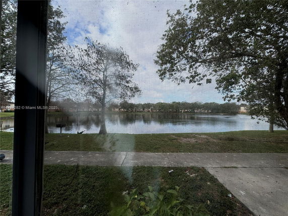 View through a screen window of a lake with trees and a pathway.