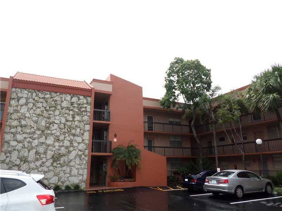 Front view of a multi-story apartment building with a stone facade and parking area.