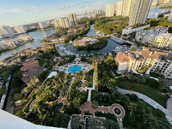 Aerial view of luxury residential area with high-rise buildings, waterways, and lush greenery.