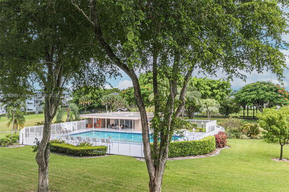 Outdoor view of a swimming pool area surrounded by a fence and trees.