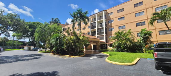 Front view of a multi-story building with a central entrance and lush greenery.