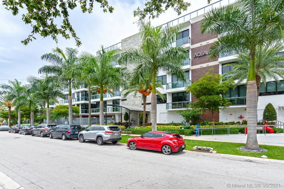 Front view of a modern multi-story building with glass balconies and palm trees.