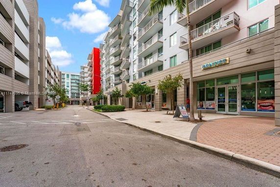 Street view of a multi-story apartment building with balconies and a commercial space on the ground floor.