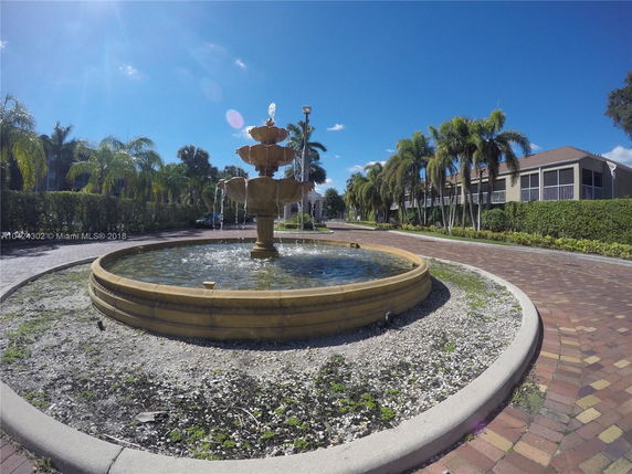 View of a landscaped area with a central decorative fountain and surrounding palm trees.