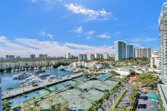 Panoramic view of a marina with boats, tennis courts, and residential high-rises.