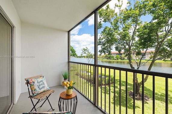 View from a balcony with a chair and small table overlooking a grassy area, trees, and a body of water.