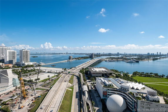Wide-angle view of a cityscape including buildings, bridges, and water bodies under a clear blue sky.