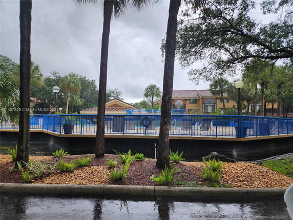 View of an exterior area with a swimming pool surrounded by blue fencing and outdoor seating, adjacent to a building.