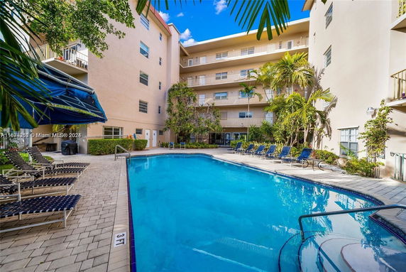 Outdoor swimming pool area with lounge chairs and surrounding multi-story building.
