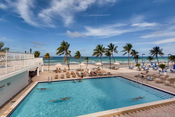 View of a beachside pool area with palm trees and ocean in the background.