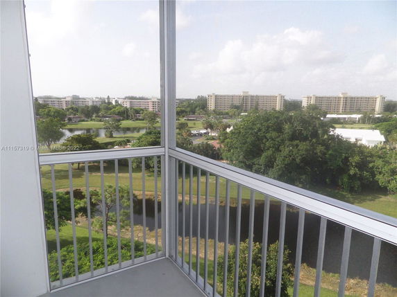 View from a balcony overlooking a landscaped area with trees and a water feature, surrounded by residential buildings.