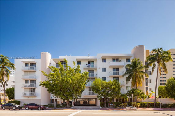 Front view of a multi-story residential building with balconies and tropical landscaping.