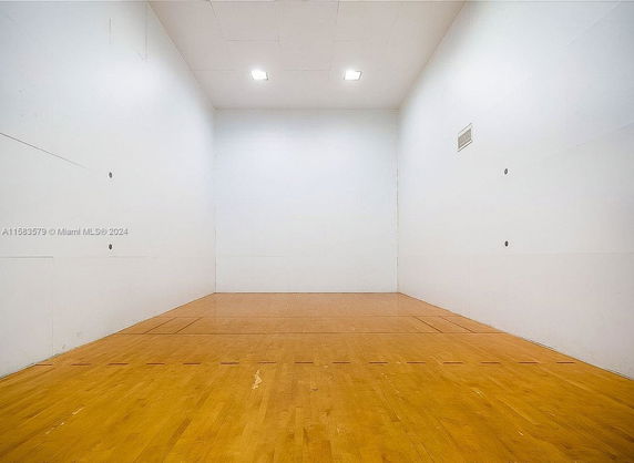 Indoor racquetball court with wooden flooring and white walls.