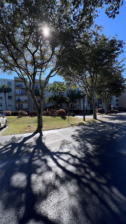 Front view of a multi-story building with balconies and large trees in the foreground.