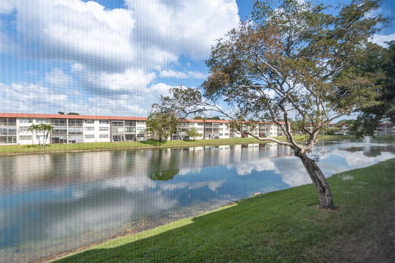View of apartment buildings across a lake with trees and grass in the foreground.