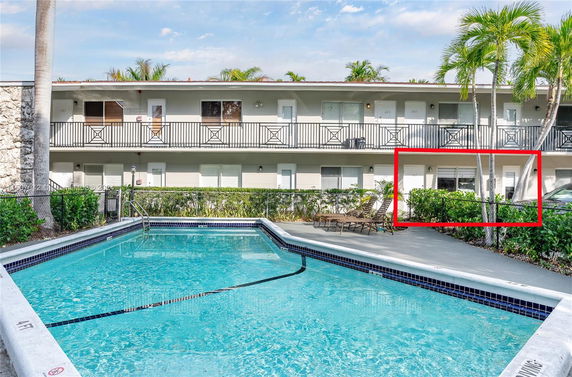 Exterior view of a multi-level building with balconies and a swimming pool in front.