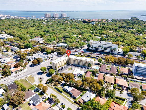 Aerial view showing a multi-story building surrounded by roads, residential houses, and greenery with a water body visible in the background.