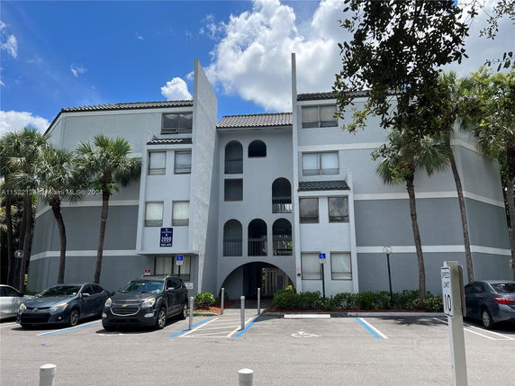 Front view of a multi-story residential building with arched windows and parking spaces.