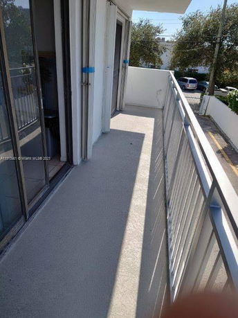 Balcony view of a white building with sliding glass doors and a metal railing.