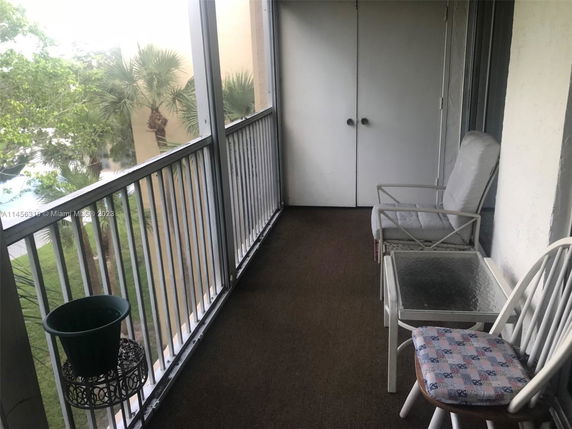 Balcony view with outdoor furniture, overlooking trees and buildings.