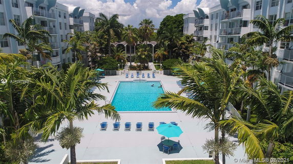 Outdoor swimming pool surrounded by lounge chairs and palm trees, with multi-story buildings in the background.
