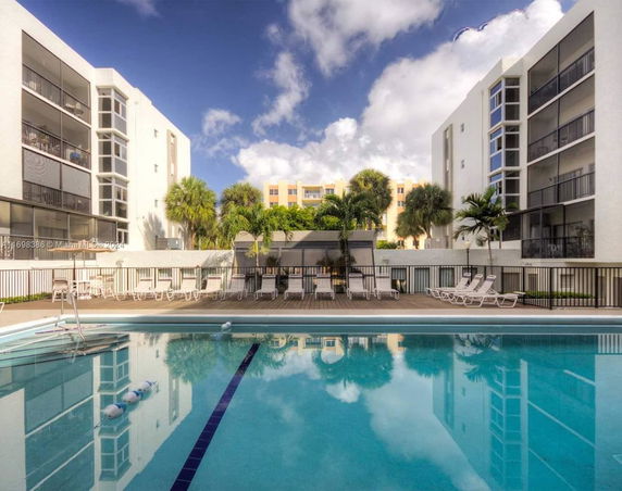 Buildings surrounding a swimming pool area with lounge chairs and a fenced deck.