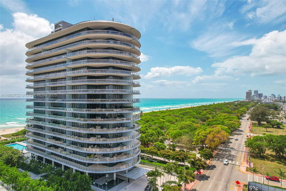 Front view of a modern, multi-story residential building with curved balconies near a beach.