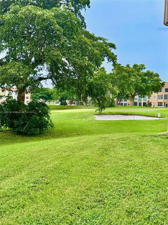 View of grassy area with trees and buildings in the background.