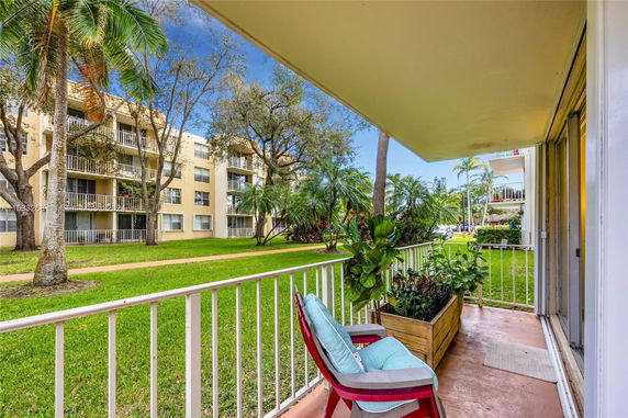 View from a balcony overlooking a green yard with a multi-story apartment building in the background.