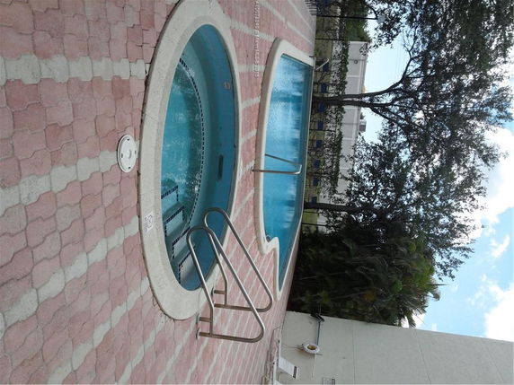 Outdoor area with a swimming pool and a circular hot tub, surrounded by a tiled patio.