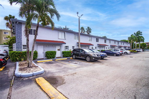 Row of townhouses with a parking area in front, featuring multiple parked cars.
