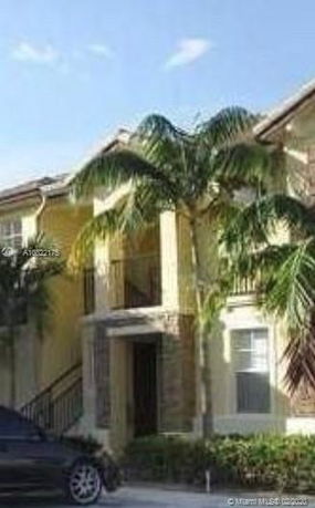 Front view of a two-story house with a balcony and palm trees.