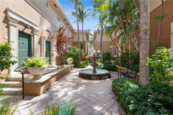 Outdoor courtyard with a fountain, surrounded by buildings with green doors and tropical plants.
