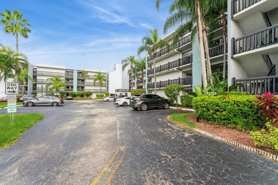 Outdoor parking area in front of multi-story buildings with cars parked under palm trees.