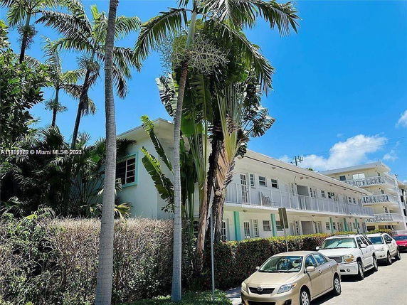 Front view of a multi-story apartment building with balconies and adjacent parking.