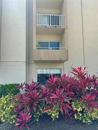 Front view of a building with balconies and shrubs in front.