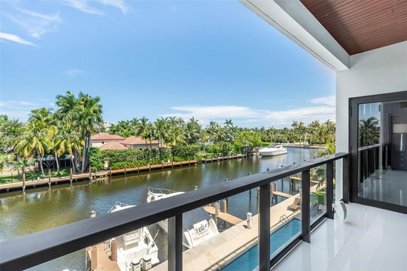 Panoramic view from a balcony overlooking a canal, lined with palm trees and a yacht.